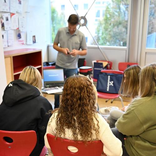 Vier weibliche Jugendliche sitzen auf roten Stühlen und hören einem Vortrag über Fußbodenheizungen zu. 