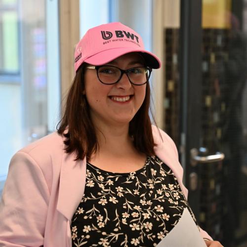 Junge Erwachsene lächelt in die Kamera. Sie trägt eine pinke Schildkappe.