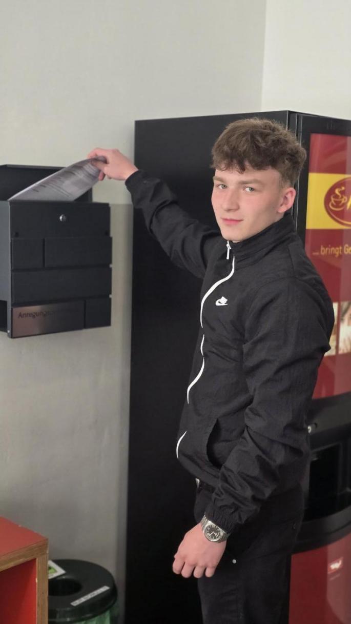 Junger Mann wirft Zettel in einen Briefkasten in seiner Schule