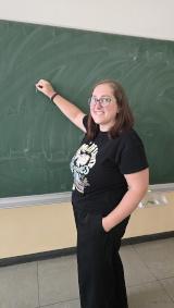 Junge Frau steht lächelnd an einer Schultafel